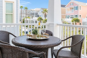 A balcony with wicker chairs and a table, a bottle of wine, and a glass. - Merri Mac Cottage | Coast Cottages Beach Access, Pool & Pavilion (Saint Simons Island)