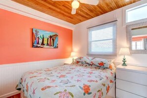 Ein Schlafzimmer mit einem Bett, einem Bild an der Wand, einem Fenster mit Jalousien und einem Deckenventilator.
