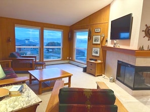 A living room with a fireplace, large windows, and a television. - Captain's Lookout 3-bedroom house in Dillon Beach perfect for relaxing getaways (Dillon Beach)