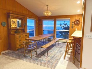 A wooden interior with a large dining table, chairs, and a bench. There are windows with a view of the outdoors. - Captain's Lookout 3-bedroom house in Dillon Beach perfect for relaxing getaways (Dillon Beach)