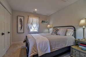 Une chambre à coucher comprenant un lit, des lampes de chevet, une table de chevet, une œuvre d’art encadrée, une fenêtre avec des rideaux et une porte.