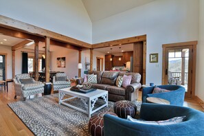 A spacious living area with a high ceiling, wooden beams, a large sofa, two armchairs, a coffee table, and a view of the kitchen and dining area. - Glorious Views 5-bedroom house in perfect Black Mountain (Black Mountain)