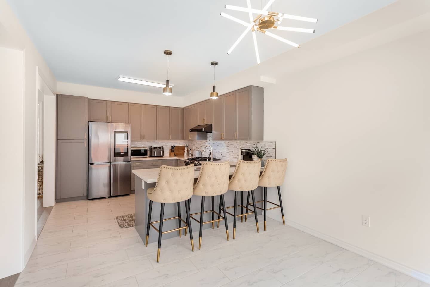 A modern kitchen with a central island, bar stools, and pendant lighting.