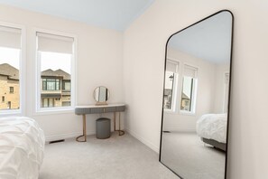 Ein Schlafzimmer mit einem großen Spiegel, einem Nachttisch, einem kleinen Hocker und einem Bett.