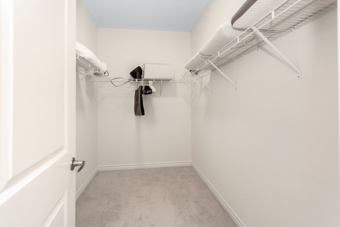 A small, enclosed room with a white door, a white ceiling, and a white wall. There is a white shelf with a hanging item and a white shelf with a white item.