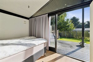 Ein Schlafzimmer mit einem Bett, einer Schiebetür zu einer Terrasse und Blick auf einen Garten.