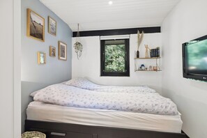 Ein Schlafzimmer mit einem Bett, einem Fenster, Wandregalen und gerahmten Bildern.
