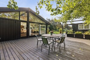 A wooden deck with a glass-enclosed patio area, outdoor seating, and a view of the surrounding garden. - Lovely Holiday Home with Hot Tub – 200m from Sea (Tranekær)