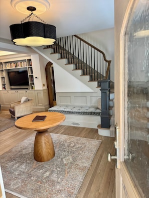 A staircase with a wooden handrail and carpeted steps, a round wooden table with a book, and a ceiling light fixture. - The Choo Choo House- Luxe renovated home w/ ADU, Sleeps 10, AC, Wrap-around Deck (Livingston)