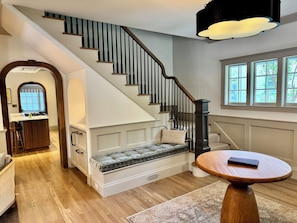 A staircase with a cushioned bench, a round wooden table, and a view of the outdoors through large windows. - The Choo Choo House- Luxe renovated home w/ ADU, Sleeps 10, AC, Wrap-around Deck (Livingston)
