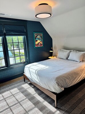 A bedroom with a large bed, a window, a wall-mounted light fixture, and a framed poster. - The Choo Choo House- Luxe renovated home w/ ADU, Sleeps 10, AC, Wrap-around Deck (Livingston)