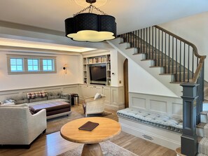 A living room with a sofa, a coffee table, a television, and a staircase. - The Choo Choo House- Luxe renovated home w/ ADU, Sleeps 10, AC, Wrap-around Deck (Livingston)