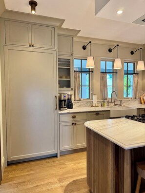 Cocina con isla central, armarios empotrados, lavamanos e iluminación colgante.