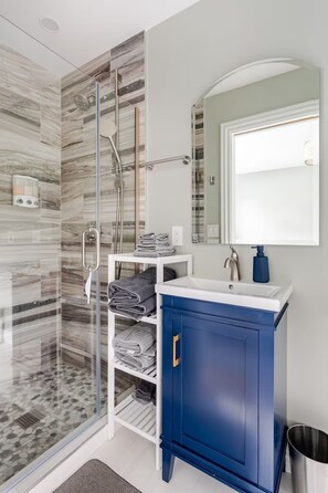 Un baño con cabina de ducha de vidrio, un lavabo blanco, un armario azul y un espejo.
