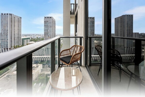 Un balcon avec deux fauteuils en osier et une table ronde, d’où l’on peut admirer une vue sur la ville, avec ses nombreux immeubles de grande hauteur.