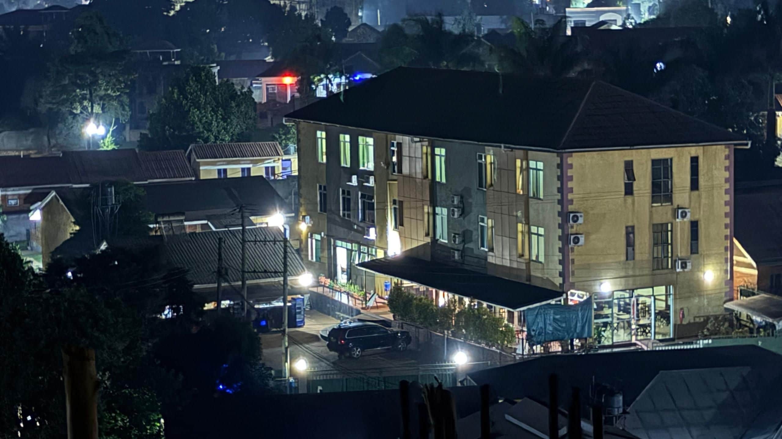 A multi-story building with a flat roof and multiple windows, surrounded by a street with parked cars and streetlights.