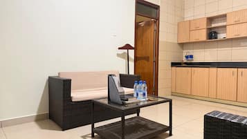 Una habitación con sofá, una pequeña mesa con una computadora portátil y una zona de cocina con armarios de madera.