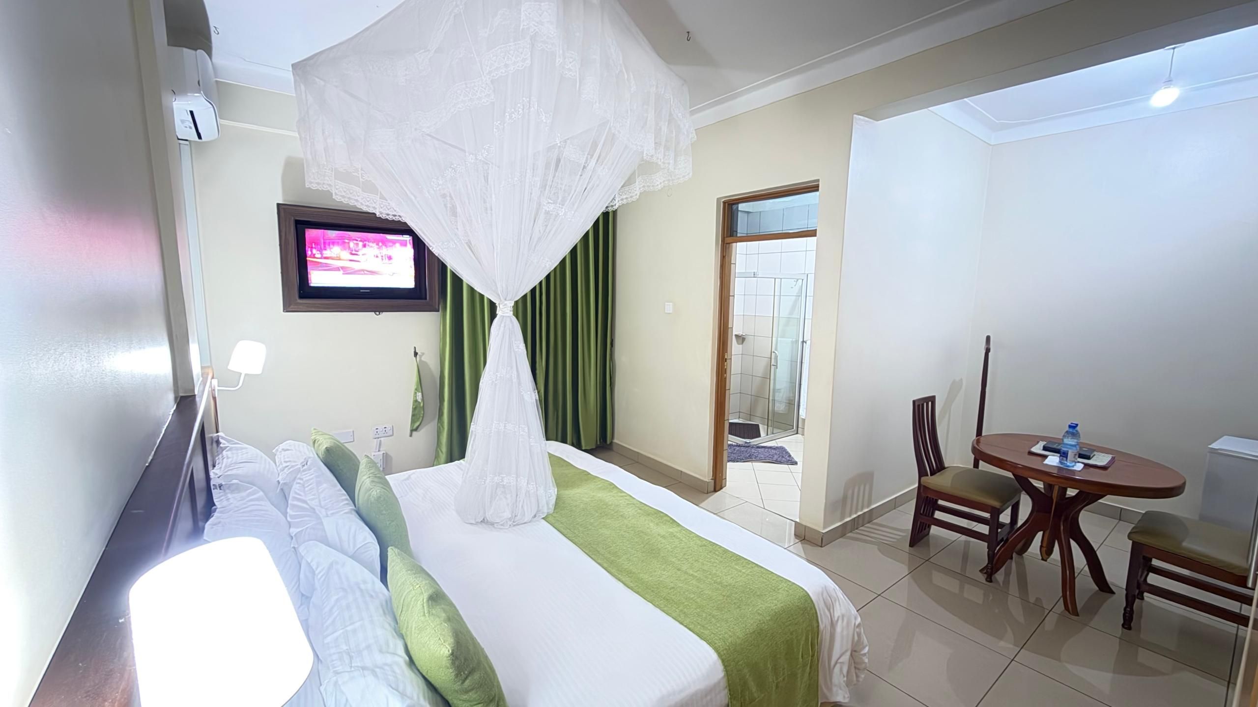 Una habitación de hotel con cama, televisor, mesa de comedor y zona de ducha.