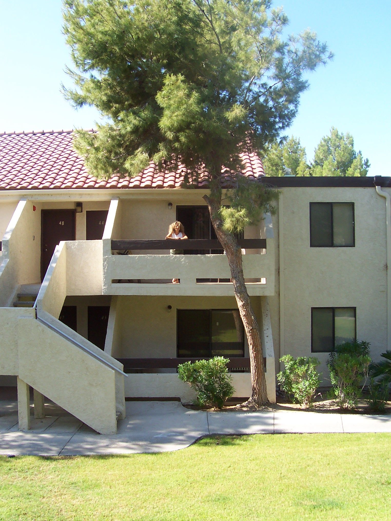A two-story building with a red-tiled roof, a staircase leading to the upper floor, and a tree in front.