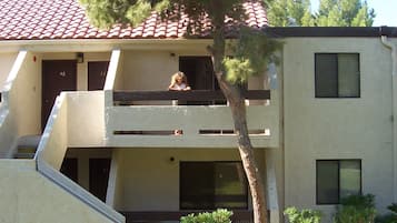 A two-story building with a red-tiled roof, a staircase leading to the upper floor, and a tree in front.