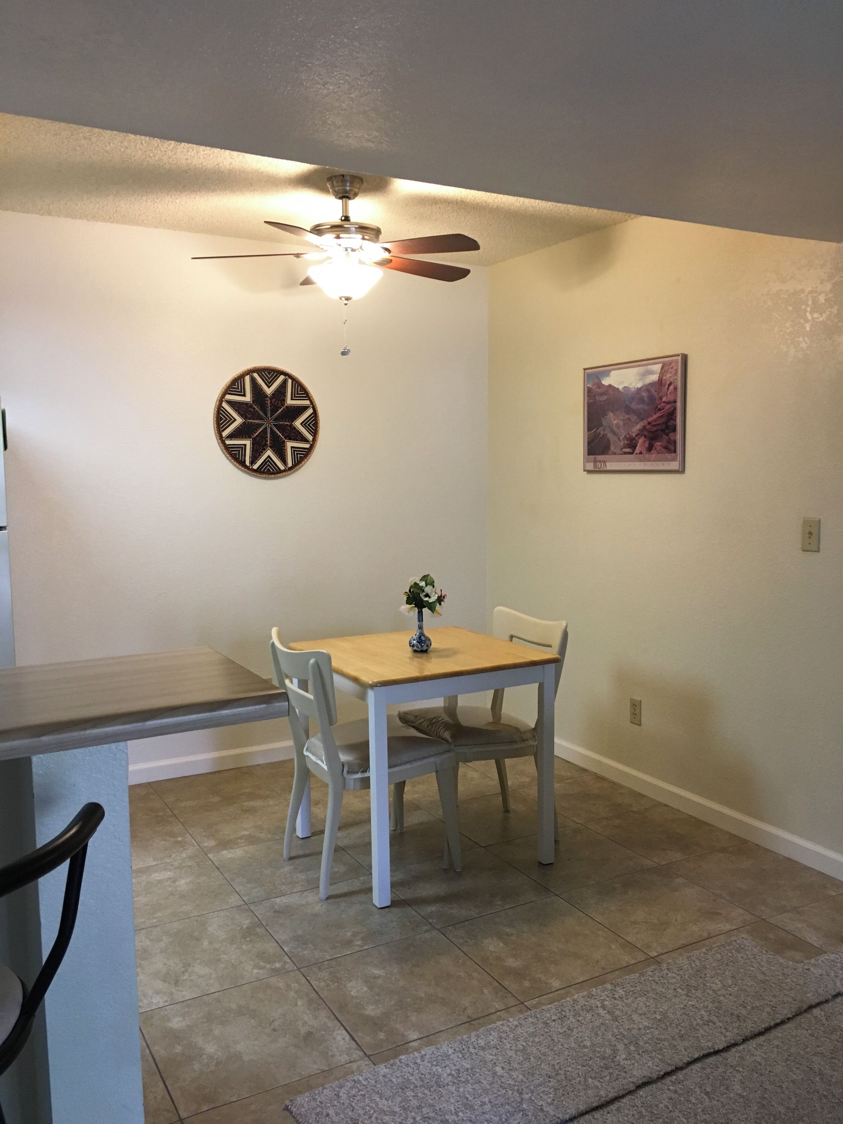 A dining area with a table, chairs, a ceiling fan, a wall-mounted light, and a framed picture.