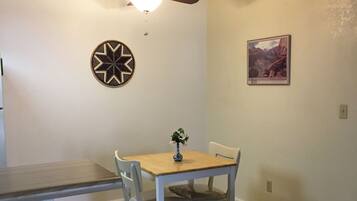 A dining area with a table, chairs, a ceiling fan, a wall-mounted light, and a framed picture.