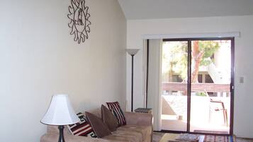 Una sala de estar con un sofá, una mesa de centro, una lámpara y un ventanal corredero que da a un área exterior.