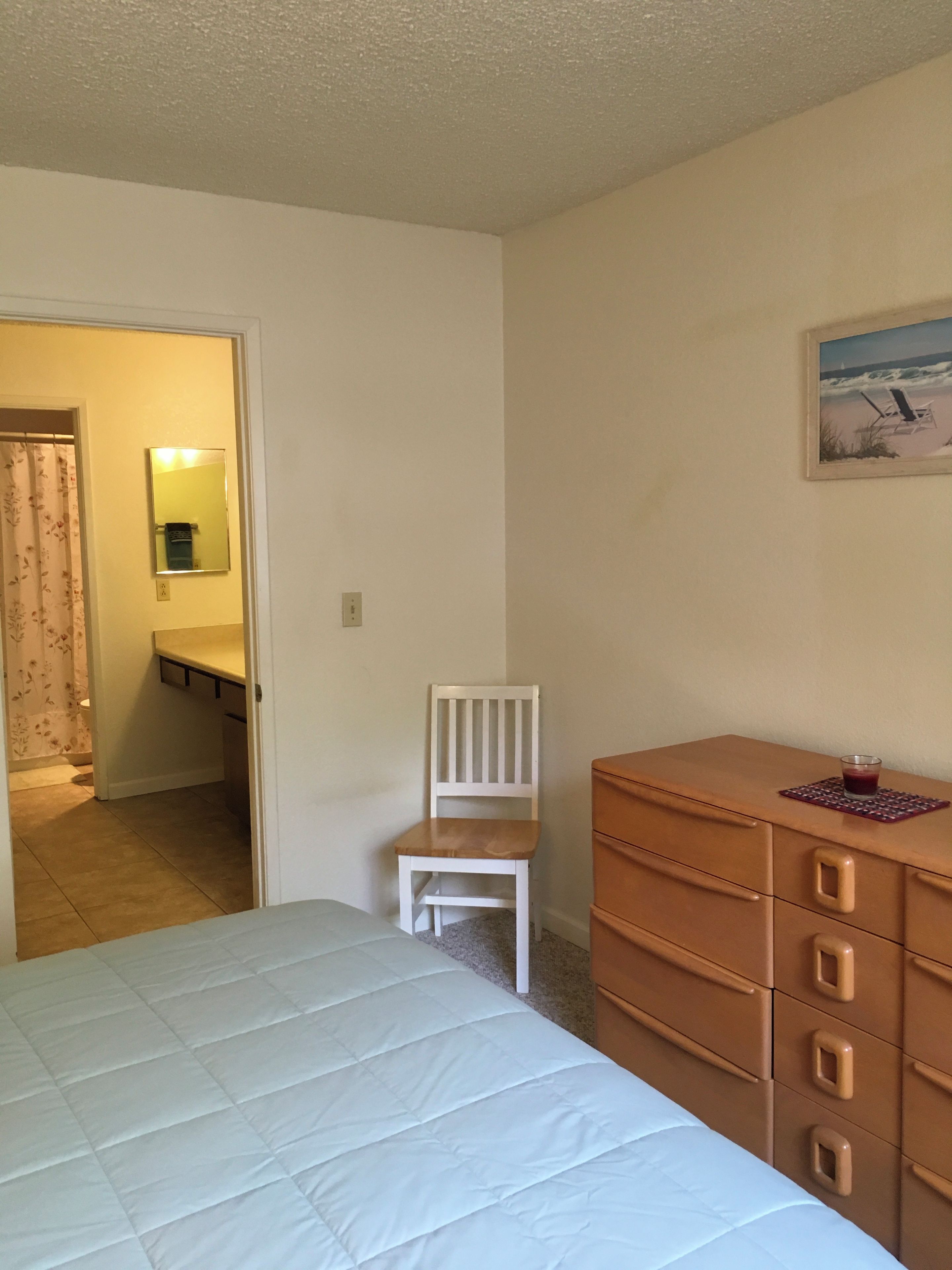 A bedroom with a bed, a wooden dresser, a chair, and a painting on the wall.