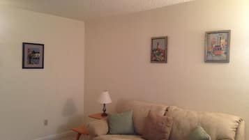 A living room with a beige sofa, a small side table, and two framed pictures on the wall.