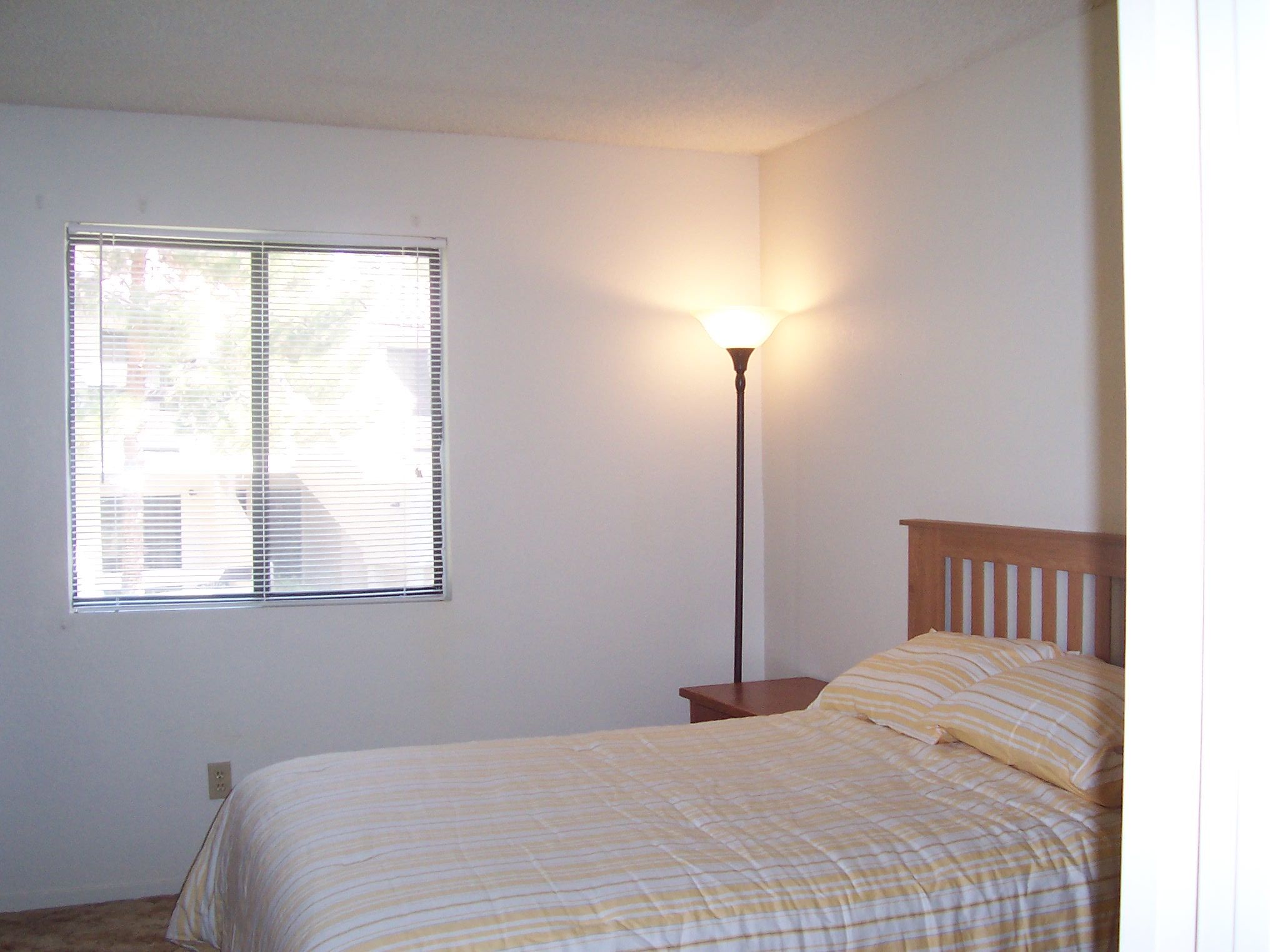 Une chambre à coucher avec un lit, une table de chevet, une lampe et une fenêtre.