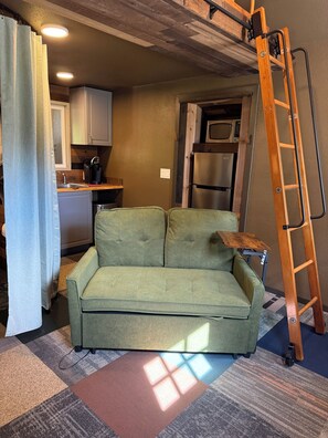 A compact living space with a sofa, a kitchen area, and a wooden ladder.