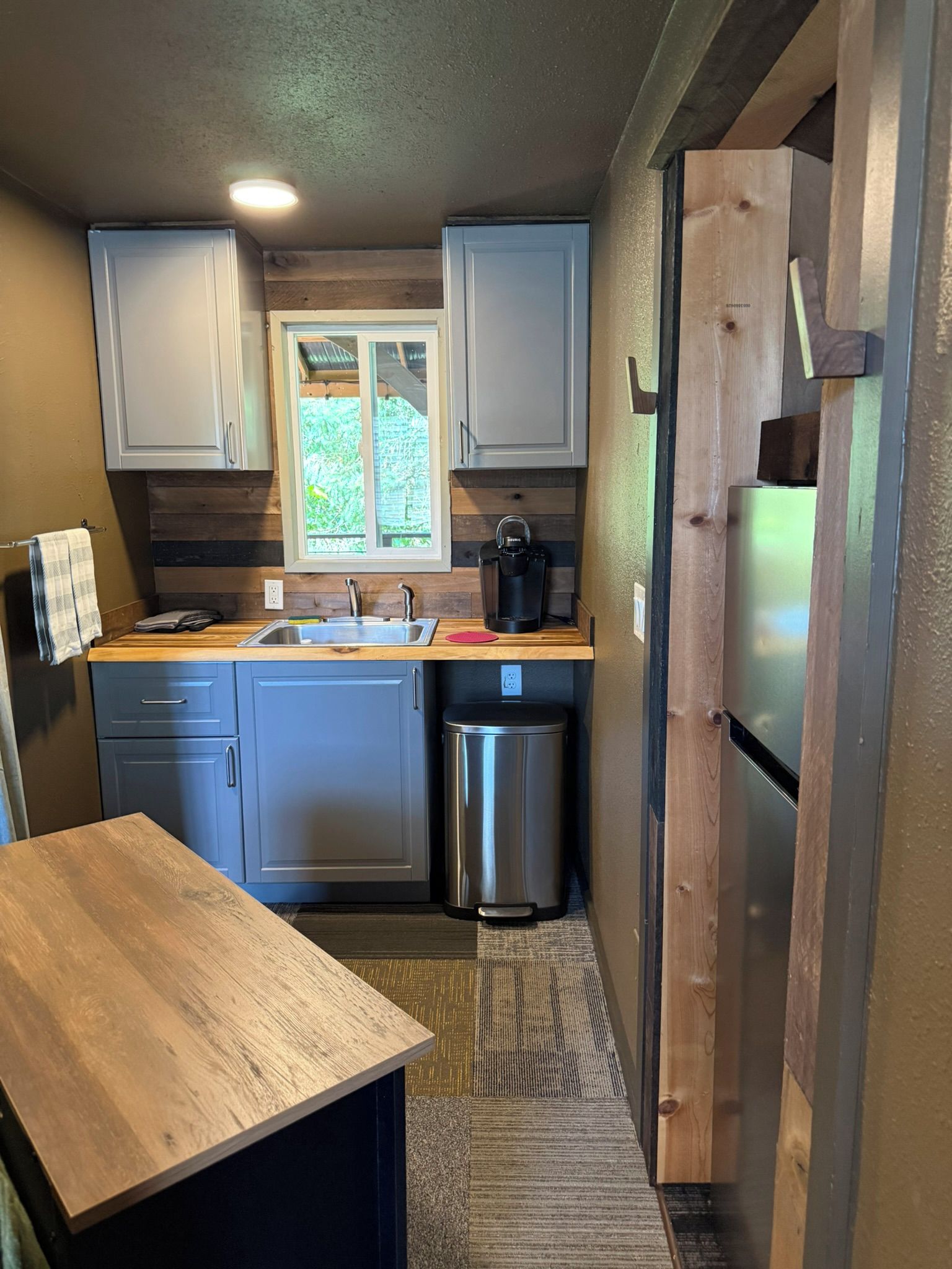 A compact kitchen with a sink, a coffee maker, and a stainless steel trash bin.