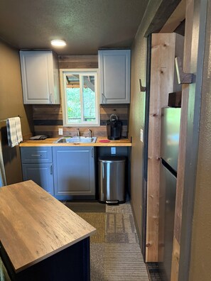 A compact kitchen with a sink, a coffee maker, and a stainless steel trash bin.