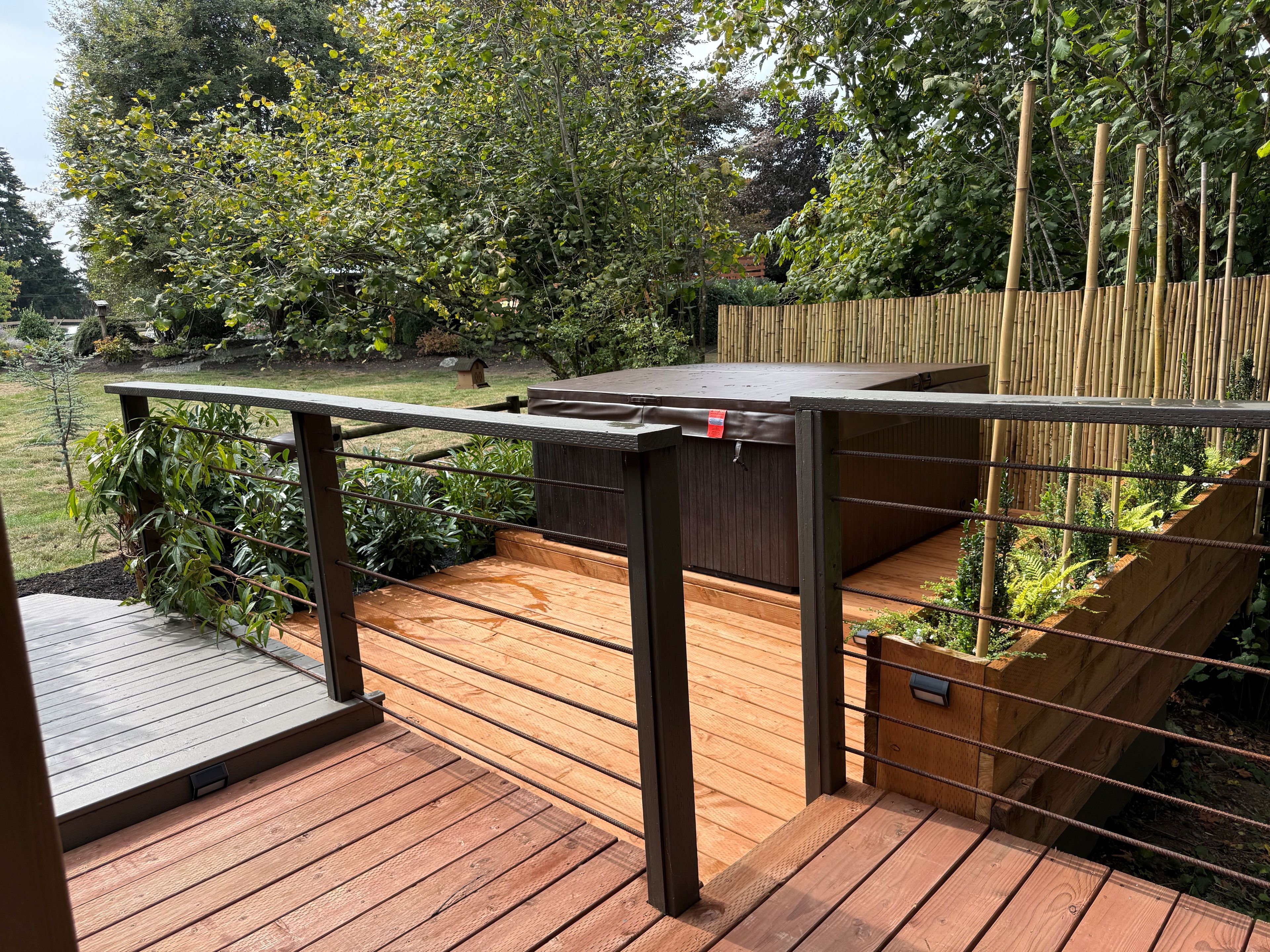 A wooden deck with a metal railing, surrounded by lush greenery and a bamboo fence.
