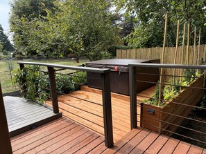 A wooden deck with a metal railing, surrounded by lush greenery and a bamboo fence.