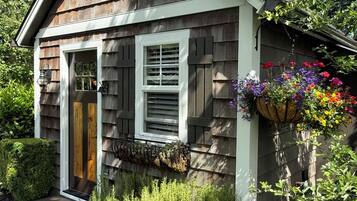 A small wooden house with a front door, two windows, and a hanging flower basket.