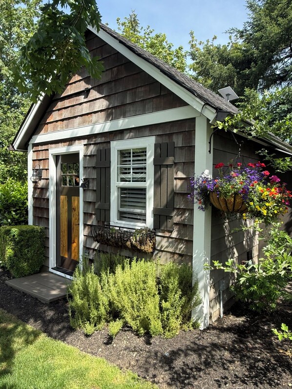 A small wooden house with a front door, two windows, and a hanging flower basket.