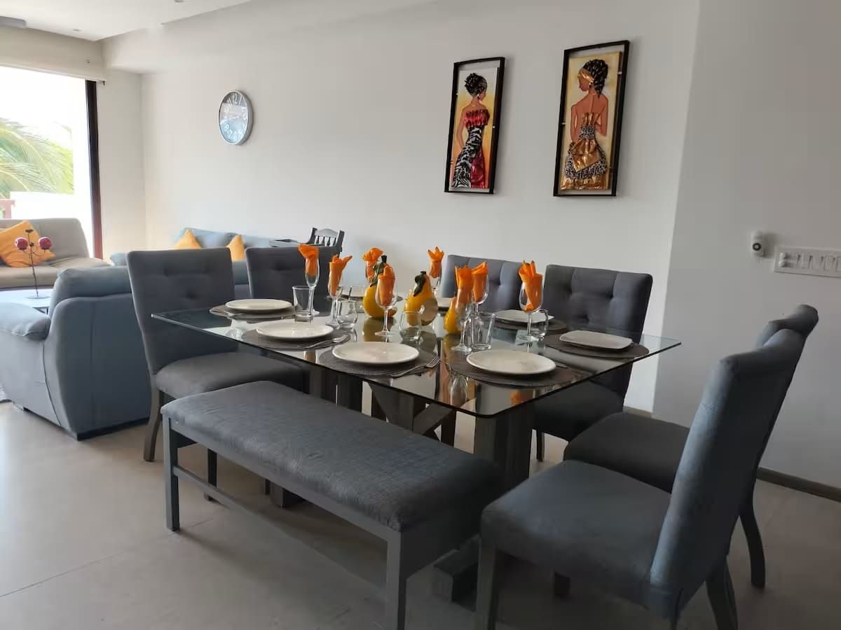 A dining area with a glass table set for four, surrounded by grey upholstered chairs.