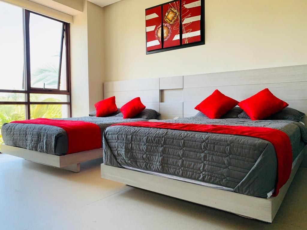 A hotel room with two beds, each with a grey and red bedspread, and a large window providing a view of palm trees.