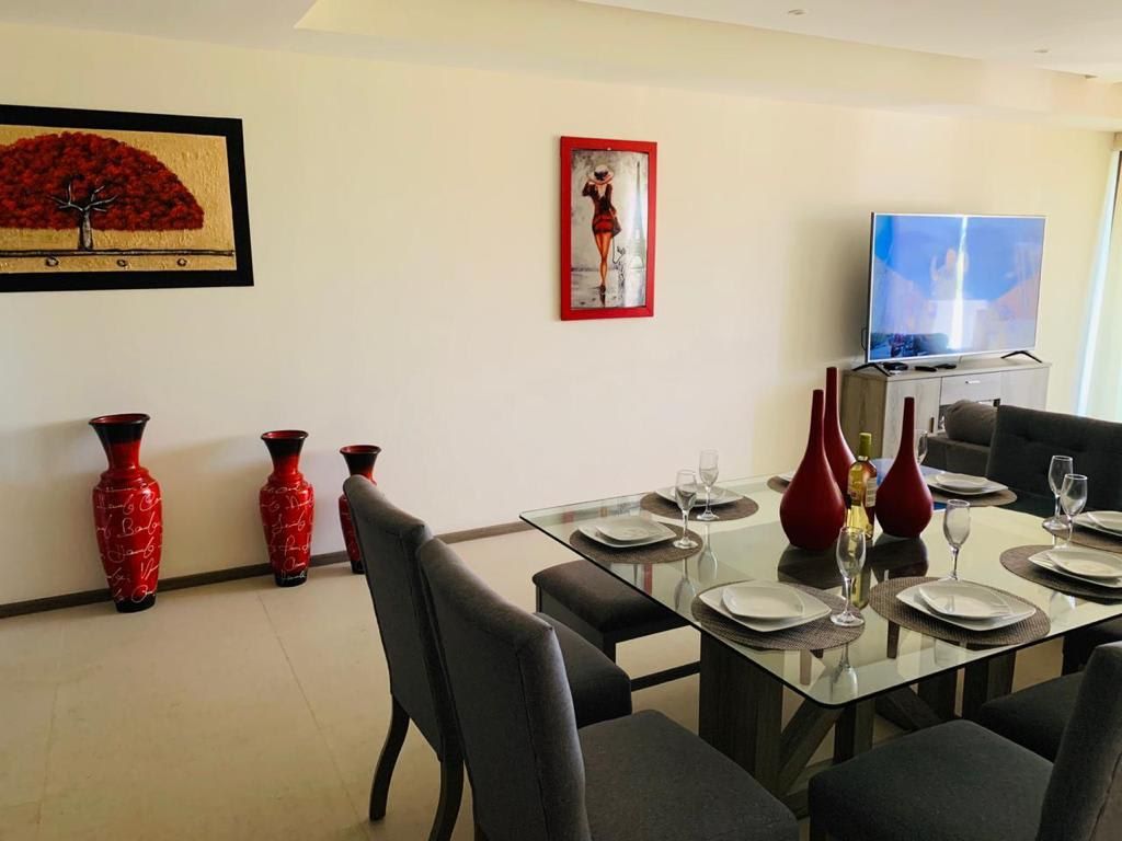 A dining area with a glass table set for four, red vases, and a framed painting on the wall.