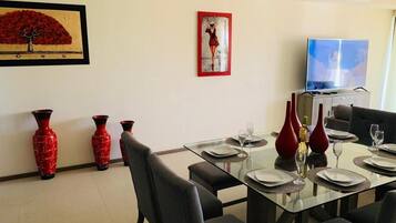 A dining area with a glass table set for four, red vases, and a framed painting on the wall.