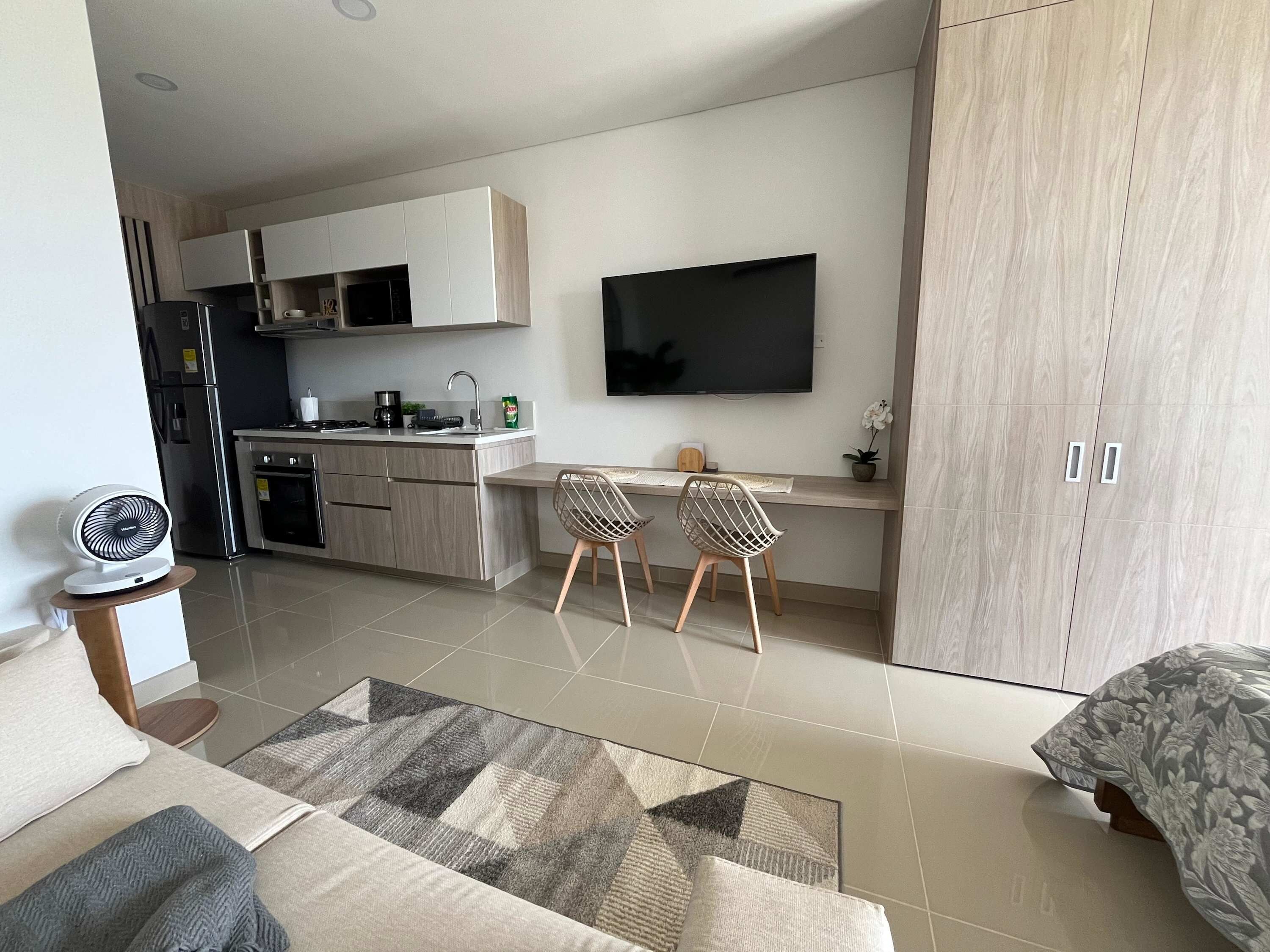A modern kitchen with a dining area, a flat-screen TV, and a sofa with a patterned rug.