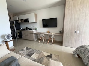 A modern kitchen with a dining area, a flat-screen TV, and a sofa with a patterned rug. - 5 Min to Beach | Rooftop Pool | Balcony (Gaira)