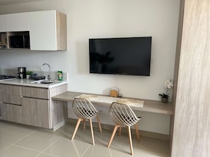 A modern kitchen with a flat-screen TV, two chairs, and a dining table. - 5 Min to Beach | Rooftop Pool | Balcony (Gaira)