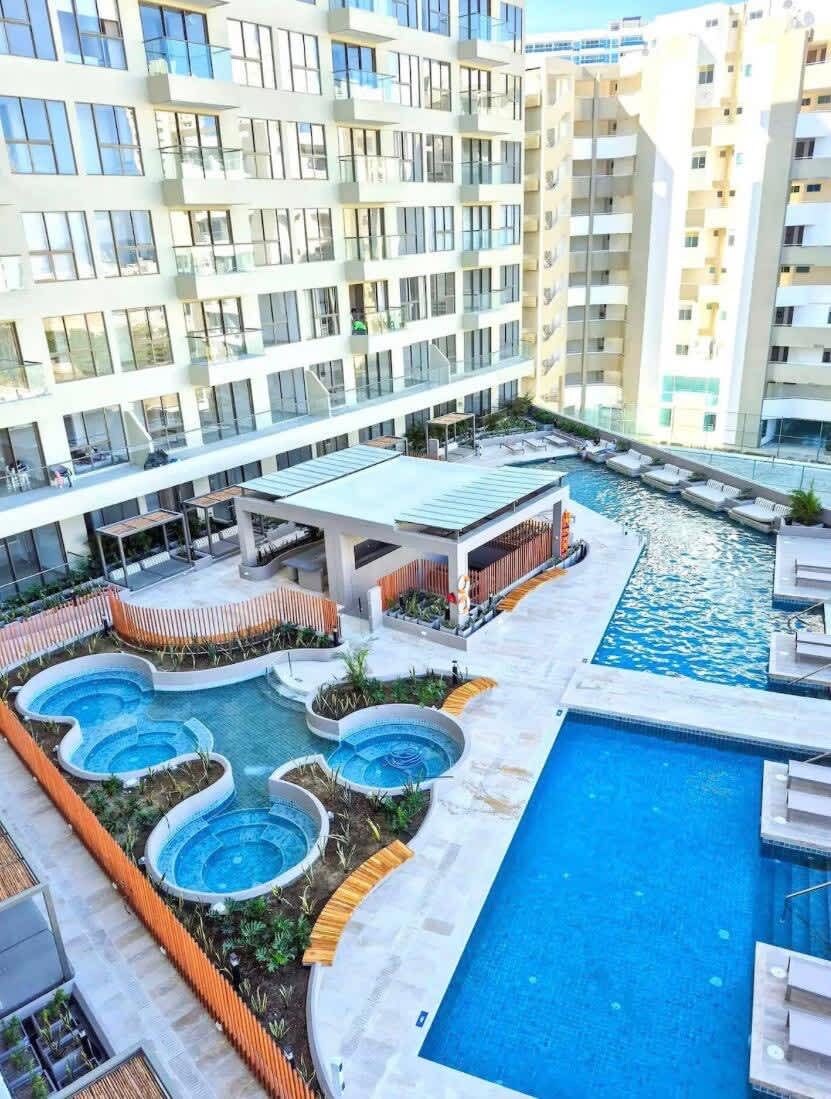 A modern hotel with multiple swimming pools, a covered seating area, and a view of adjacent high-rise buildings.