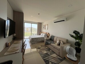 A modern hotel room with a bed, a sofa, a TV, and a balcony with a view of a cityscape. - 5 Min to Beach | Rooftop Pool | Balcony (Gaira)