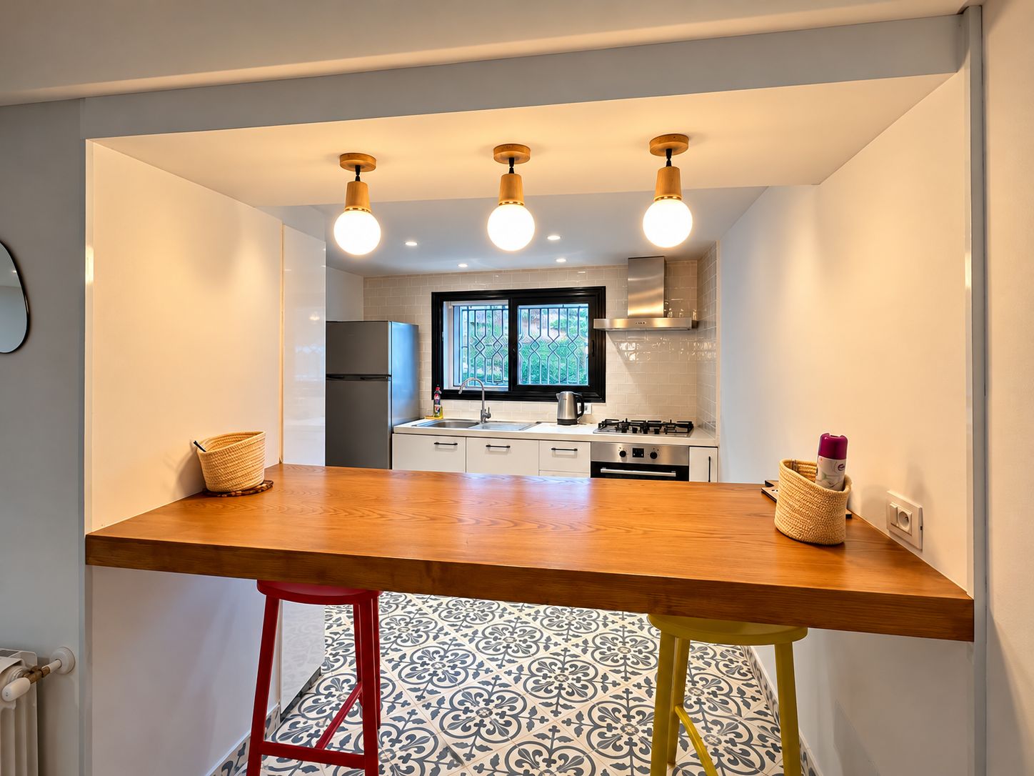 Cocina compacta con encimera de madera, refrigerador, ventana con celosía decorativa y estufa a gas.