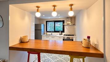 Cocina compacta con encimera de madera, refrigerador, ventana con celosía decorativa y estufa a gas.