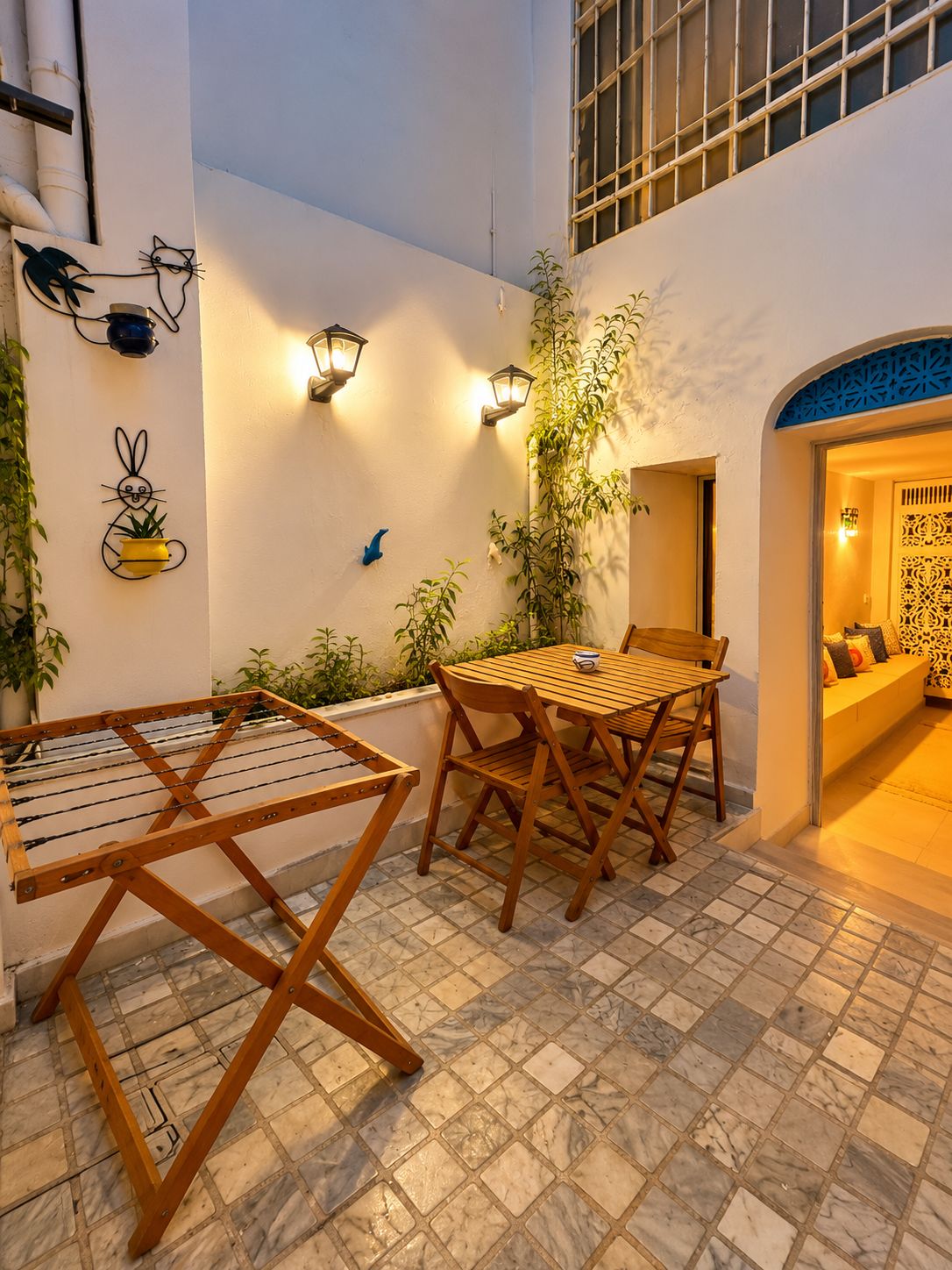 Un área de estar al aire libre con una mesa y sillas de madera, un tendedero y luces fijadas a la pared.