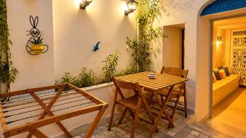 Un área de estar al aire libre con una mesa y sillas de madera, un tendedero y luces fijadas a la pared.